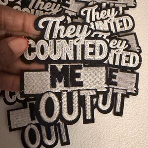 May include: Embroidered patches with the phrases "They Counted Me Out" and "They Counted Me In". The patches are black with white embroidered text and a white border. The patches are rectangular and have a cursive font.
