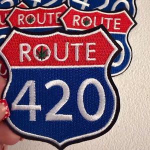 May include: A shield-shaped embroidered patch featuring a red top section with the white text ROUTE and a green leaf icon, and a blue bottom section with the large white number 420. The patch has a thick black border and is stacked with others.