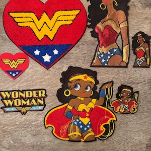 May include: A collection of embroidered patches featuring Wonder Woman imagery, including a large heart-shaped logo, a text patch reading Wonder Woman, and various character depictions in red, blue, gold, and white thread on a wooden surface.
