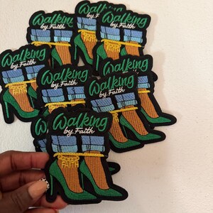 May include: A collection of embroidered patches featuring a pair of green high-heeled shoes, blue denim pant cuffs, and a gold chain anklet with the word FAITH. The text Walking by Faith is embroidered in green above the shoes on each patch.