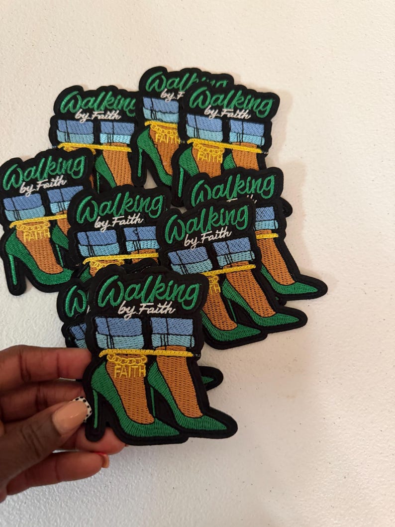 May include: A collection of embroidered patches featuring a pair of green high-heeled shoes, blue denim pant cuffs, and a gold chain anklet with the word FAITH. The text Walking by Faith is embroidered in green above the shoes on each patch.