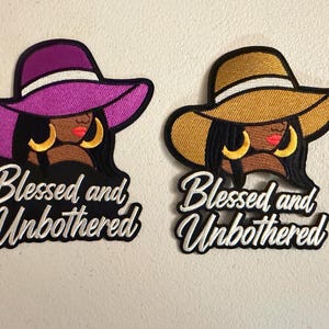 May include: Two embroidered patches featuring a person wearing a wide-brimmed hat and large hoop earrings. One hat is purple, the other is gold. Both patches display the white embroidered text Blessed and Unbothered on a black background.