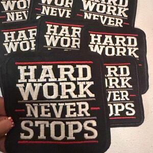 May include: Black embroidered patches with the words "HARD WORK NEVER STOPS" in white and gray lettering. The patches have a red border and are square-shaped. The patches are stacked on top of each other.