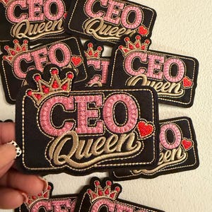 May include: A collection of rectangular black embroidered patches featuring the text CEO QUEEN in pink and gold thread. Each patch includes a red and gold crown icon above the text and a small red heart icon to the right of the word QUEEN.
