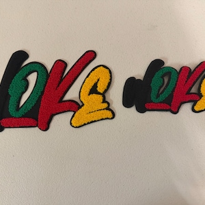 May include: Two embroidered patches with the word "woke" in a stylized font. The letters are black, green, red, and yellow. The patches are on a white surface.