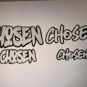 May include: Four white fabric patches with the word "CHOSEN" in a bubble letter style with a black outline. The patches vary in size and are displayed on a white background.