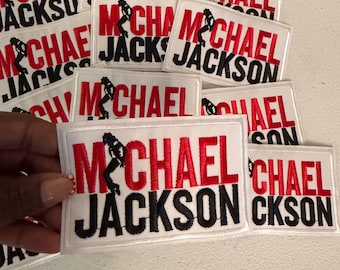 May include: A collection of rectangular white embroidered patches featuring the text Michael Jackson in red and black thread. Each patch includes a small black silhouette of a dancer in a signature pose integrated into the letter M.