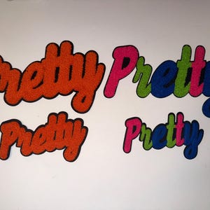 May include: Four embroidered patches with the word "Pretty" in a script font. Two patches are orange with black outlines, and two are multi-colored with pink, green, and blue lettering.