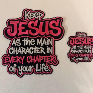 May include: Two embroidered patches with the text "Keep JESUS as the MAIN CHARACTER IN EVERY CHAPTER of your Life." The patches have a black background with pink and white lettering.