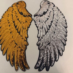 May include: Two large wing-shaped patches featuring dense, shimmering sequin embroidery. One wing is covered in metallic gold sequins, while the other is covered in bright silver sequins. Both patches have a black fabric border outlining the feathers.