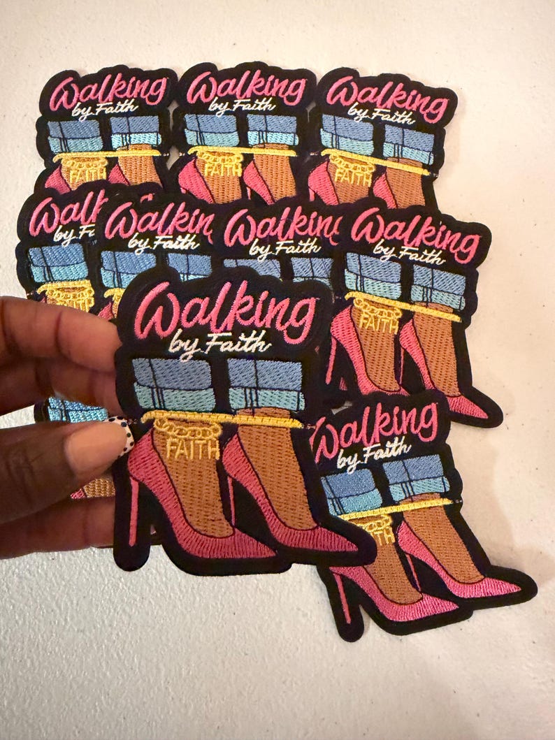 May include: A collection of embroidered patches featuring a graphic of legs in blue jeans and pink high heels with a gold ankle chain that says FAITH. The text Walking by Faith is embroidered in pink and white above the legs on a black background.
