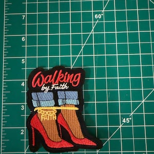 May include: An embroidered patch featuring red high-heeled shoes, blue denim pant cuffs, and a gold ankle chain with the word FAITH. The text WALKING by Faith is stitched in red and white above the shoes. The patch measures 3.5 inches tall.