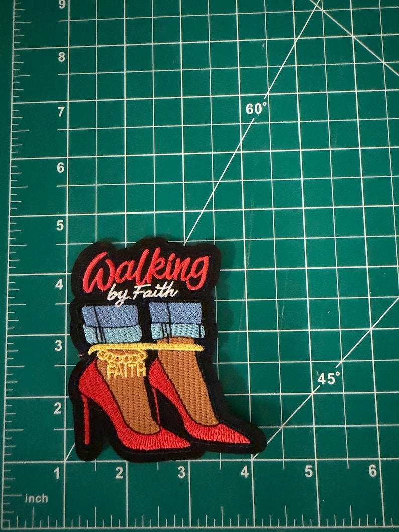 May include: An embroidered patch featuring red high-heeled shoes, blue denim pant cuffs, and a gold ankle chain with the word FAITH. The text WALKING by Faith is stitched in red and white above the shoes. The patch measures 3.5 inches tall.