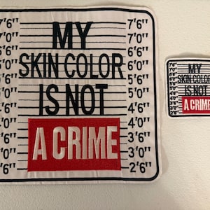 May include: Two white patches with black text and a red rectangle. The larger patch reads "MY SKIN COLOR IS NOT A CRIME" with height markings in feet and inches. The smaller patch has the same text and design.
