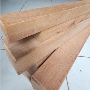 Könnte beinhalten: Ein Stapel unbearbeiteter rechteckiger Holzbretter. Die Bretter sind hellbraun und weisen eine sichtbare Holzmaserung auf. Das Holz scheint frisch geschnitten und bereit für den Einsatz in einem Bau- oder Holzbearbeitungsprojekt zu sein.