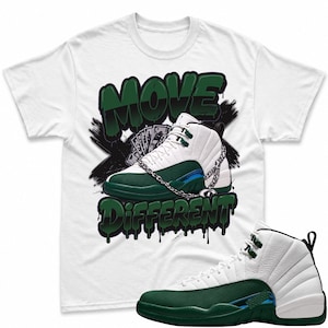 May include: A white short-sleeve t-shirt featuring a graphic of a white and dark green sneaker with a silver chain, a fan of dollar bills, and the text MOVE DIFFERENT in dark green graffiti-style lettering, accompanied by a matching sneaker.