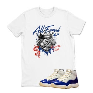 May include: White t-shirt with a graphic design featuring a crown, money, and the text "All Earned" and "Respect the Hustle" in blue and red. A pair of white and blue sneakers are at the bottom.