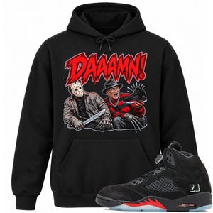 May include: A black hooded sweatshirt featuring a graphic print of Jason Voorhees and Freddy Krueger with the text DAAAMN! above them. The characters are depicted holding a black and red high-top sneaker, matching the sneaker shown below.