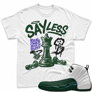 May include: A white short-sleeve t-shirt featuring a dark green graphic of a chess queen and pawns with the text "SAY LESS" and "REAL ONES MOVE IN SILENCE" in purple, paired with a white and dark green high-top sneaker with a textured leather finish.