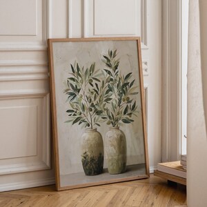 Könnte beinhalten: Ein gerahmter, vertikaler Kunstdruck, der zwei strukturierte, helle Keramikvasen zeigt. In jeder Vase steckt ein belaubter Olivenzweig mit kleinen grünen Oliven. Der Hintergrund des Gemäldes weist eine neutrale, cremeweiße Pinselstrich-Optik auf.