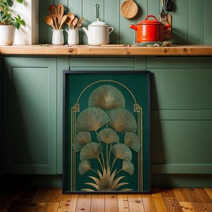 May include: A framed art print featuring a gold botanical design on a dark green background. The artwork has a black frame and is displayed in a kitchen setting with green cabinets and wooden countertops.