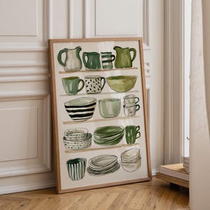 Puede incluir: Una lámina artística enmarcada que muestra una colección de utensilios de cocina verdes y blancos, incluyendo jarras, cuencos y tazas dispuestos en estantes. La ilustración utiliza pinceladas sueltas y tonos verdes para los objetos.