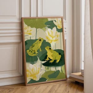 May include: A framed art print depicting two green frogs on lily pads, with yellow and white water lilies. The background is light green, and the frame is natural wood. The artwork is suitable for a living room.
