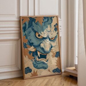 May include: A rectangular framed wall art print featuring a stylized blue Hannya mask with sharp teeth and piercing yellow eyes. The illustration is surrounded by orange maple leaves and dark blue cloud motifs set against a light beige background.