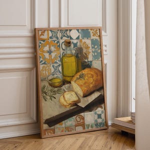 Puede incluir: Una lámina artística rectangular enmarcada que muestra un bodegón con una botella de cristal llena de aceite de oliva amarillo, un cuenco pequeño con aceite y un pan crujiente con romero, sobre un fondo de azulejos azules, blancos y amarillos.