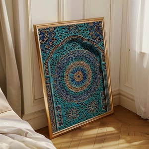 May include: A framed, ornate wall art piece with a gold-coloured frame. The artwork features a detailed, carved design in shades of teal, blue, and gold. The intricate pattern includes floral and geometric elements, creating a layered, three-dimensional effect. The artwork is leaning against a white wall.