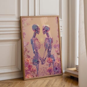 May include: A framed art print featuring two stylized skeletons holding hands, facing each other. The skeletons are in shades of blue and purple, set against a soft pink background with floral accents. The artwork is in a wooden frame.
