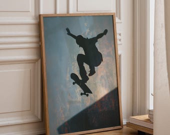 May include: A rectangular framed wall art print featuring a dark silhouette of a person performing a jump on a skateboard. The background displays a textured, weathered surface with muted blue and orange tones, set within a light wood frame.