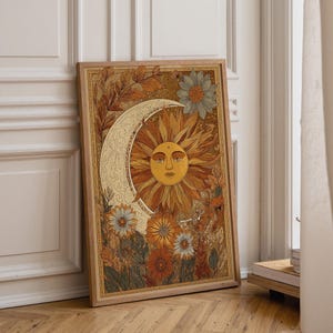 Puede incluir: Una lámina de arte mural rectangular enmarcada que presenta un sol central con rostro humano rodeado por una luna creciente y elementos florales en tonos naranja, amarillo, marrón y verde sobre un fondo dorado texturizado.