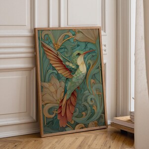 May include: A framed art print depicting a hummingbird in flight. The bird has teal, orange, and white feathers, set against a teal and gold background with floral and swirling patterns. The frame is made of light-coloured wood.