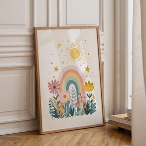 Può includere: Una stampa artistica incorniciata raffigurante un arcobaleno centrale, un sole giallo e stelle sparse sopra un giardino di fiori e fogliame rosa, giallo e blu. L'illustrazione utilizza una tavolozza di colori tenui su uno sfondo color crema.