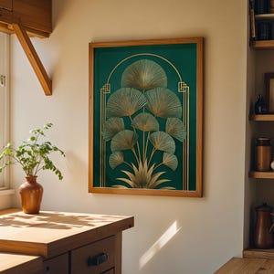 May include: A framed art print featuring a botanical design with gold fan-shaped leaves on a dark green background. The artwork is in a wooden frame and hangs on a white wall. The image is in a well-lit room with a wooden countertop and a window.