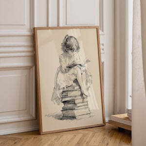 以下が含まれることがあります： ベージュの背景に黒いインクで描かれたスケッチの額入りアートプリント。ウェーブのかかった髪でドレスを着た子供が、積み上げられた高い本の上に座り、手にした開いた本を読んでいる様子が描かれています。