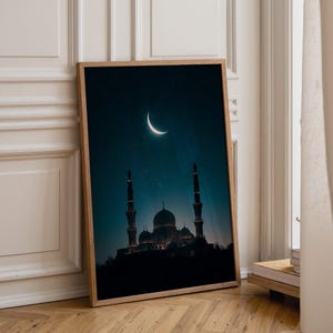 May include: A rectangular framed wall art print featuring a dark blue night sky with a glowing crescent moon above the silhouette of a mosque with a central dome and two tall minarets. The artwork is encased in a light-toned wooden frame.
