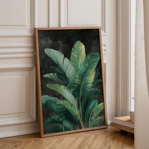May include: A rectangular framed wall art print featuring a detailed illustration of large, vibrant green banana leaves set against a dark, moody charcoal grey background. The wooden frame has a natural light brown finish and clean edges.