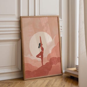 Puede incluir: Una lámina de arte vertical enmarcada que muestra la silueta de una persona en postura de árbol de yoga frente a un gran sol pálido y nubes superpuestas de color terracota. La obra utiliza una paleta de tonos tierra cálidos.