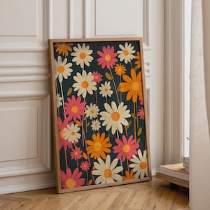 May include: A rectangular framed wall art print featuring a dark navy blue background covered in a repeating pattern of stylised daisies in shades of cream, bright orange, and vibrant pink, each with a yellow centre and thin green stems.