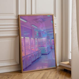 Op de afbeelding: Een rechthoekige ingelijste muurkunstprint met een rij verlichte grijpmachines in een kamer die baadt in levendig paars en talingkleurig neonlicht. De scène toont een reeks arcadekasten met glazen fronten en oplichtende displays.