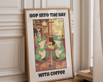 May include: A framed wall art print featuring two green frogs sitting at a small table in a cafe setting, each holding a white mug. The text at the top reads HOP INTO THE DAY and the text at the bottom reads WITH COFFEE in bold black letters.
