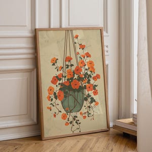 Pode incluir: Uma impressão artística emoldurada com uma planta suspensa com flores laranja e folhas verdes. A planta está num vaso verde-azulado, suspensa por cordas castanhas sobre um fundo amarelo claro. A moldura é de madeira.