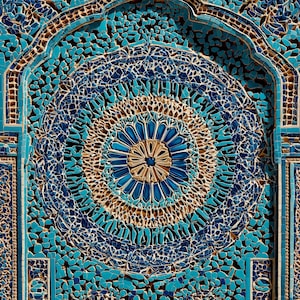 May include: Detailed mosaic wall with a central circular design. The artwork uses shades of blue, beige, and turquoise, with a mosaic of small, irregular pieces. The design is ornate and detailed, showcasing a complex pattern.