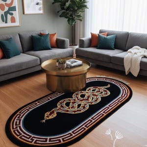 Puede incluir: Alfombra ovalada negra con un diseño detallado de serpiente en tonos rojos, dorados y azules. La alfombra tiene un borde estampado y está colocada en un salón con sofás grises y una mesa de centro dorada.