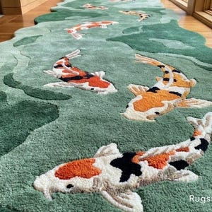 May include: A green, river-shaped rug featuring several koi fish in shades of orange, white, and black. The rug has a textured surface and is placed on a wooden floor. The rug's design mimics a flowing river.