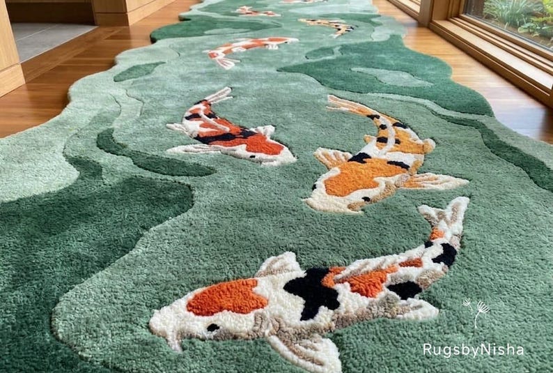 May include: A green, river-shaped rug featuring several koi fish in shades of orange, white, and black. The rug has a textured surface and is placed on a wooden floor. The rug's design mimics a flowing river.