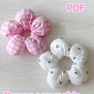 Könnte beinhalten: Zwei blütenförmige Haargummis. Eines ist rosa und weiß kariert, das andere ist weiß mit kleinen schwarzen Kirschmustern. Das Wort "PDF" befindet sich in der oberen rechten Ecke. Die Worte "flower scrunchie" stehen unten.