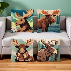 May include: Four square throw pillows featuring textured punch needle designs of moose in various forest settings. The pillows display brown moose with large antlers against backgrounds of green trees, blue water, and white flowers, with one moose wearing a scarf.